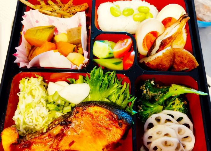 An overhead shot of a colorful bento box, filled with fresh veggies, rice, and salmon.